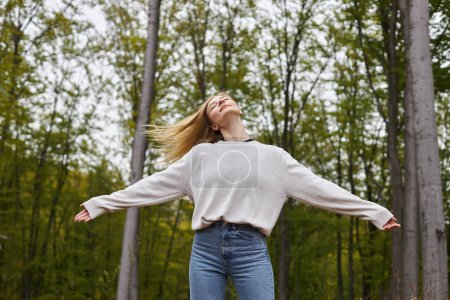 Photo for Peaceful and relaxed blonde woman dancing in forest jeans and sweater on backpacking trip - Royalty Free Image