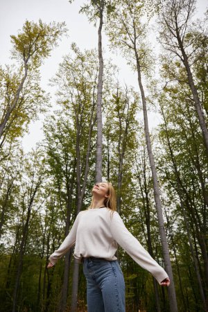 Foto de Meditar chica rubia en acogedor, suéter senderismo en el bosque y tener un momento tranquilo con los ojos cerrados - Imagen libre de derechos