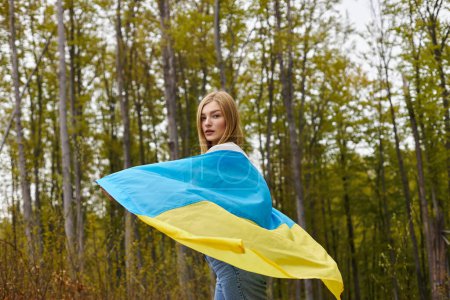 Rückansicht einer jungen blonden Wanderin, die die ukrainische Flagge hält und sich der Kamera zuwendet