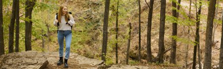 Blonde Wanderin mit Rucksack wandert durch den Wald und entdeckt neue Wege