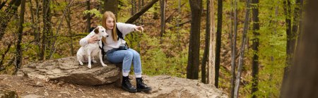 Téléchargez les photos : Aventurière blonde dévouée montrant à son chien curieux une direction assise sur un rocher dans les bois, bannière - en image libre de droit