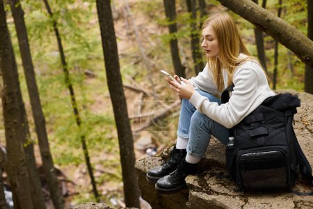 Foto de Vista lateral de la mujer sosteniendo el teléfono mientras descansa en el bosque. Concepto de senderismo y turismo - Imagen libre de derechos
