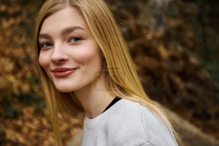 Portrait of smiling beautiful blonde woman looking at the camera while walking in forest