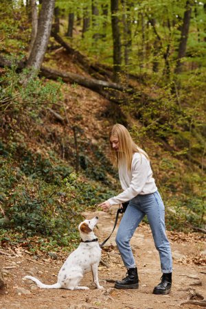 Happy girl interact with her pet holding leash at hiking rest with mountain and forest view