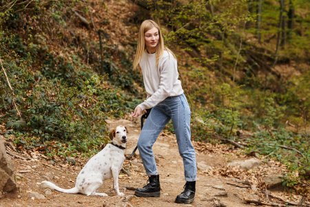 Young woman training her pet dog holding leash at hiking rest with mountain and forest view