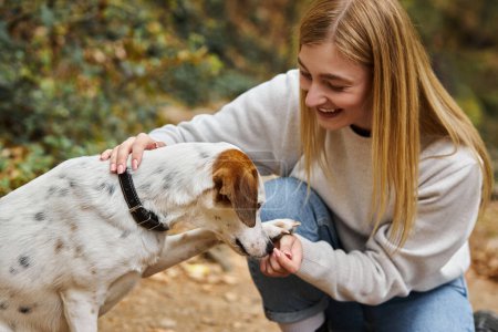 Laughing woman training her pet dog while having backpacking trip with companion