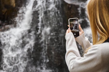Rückansicht einer Frau, die majestätische Wasserfälle im Wald fotografiert, Wander- und Sightseeing-Konzept