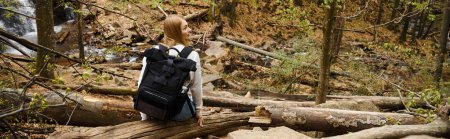 Foto de Vista posterior de la joven senderista rubia con mochila sentada y descansando durante el trekking, pancarta - Imagen libre de derechos