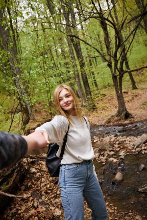 Porträt einer lächelnden jungen Frau, die die Hand ihres Freundes hält, während sie im Wald spaziert