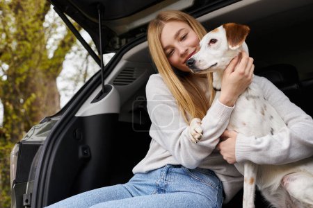 Chica feliz interactuando con su mascota mirando al perro en el descanso de senderismo se detiene en la parte trasera del coche