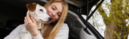 Foto de Chica feliz interactuando con su mascota mirando al perro en el descanso de senderismo parada en la parte trasera del coche, pancarta - Imagen libre de derechos