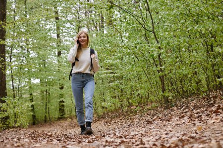 Full length photo of woman traveler with backpack talking by phone walking in forest path