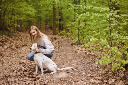 Foto de Chica senderista sonriente interactuando con su mascota mirando hacia la dirección mientras camina descanso con vista al bosque - Imagen libre de derechos