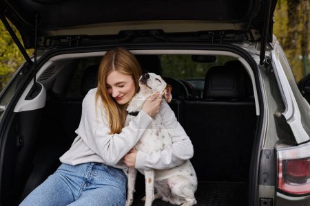 Photo for Image of woman gently hugging her white dog sitting at back of car. Dog companion - Royalty Free Image