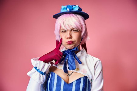 appealing young female cosplayer with red gloves and blue hat posing emotionally on pink backdrop