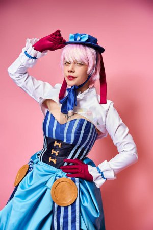 alluring sexy female cosplayer in blue hat and vibrant attire looking at camera on pink backdrop