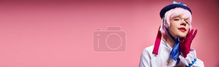 seductora cosplayer femenina en sombrero azul y ropa vívida mirando a la cámara en el fondo rosa, pancarta