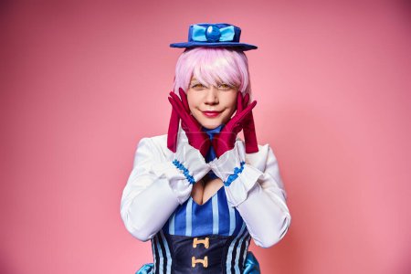 fashionable chic female cosplayer in blue hat and vivid dress looking at camera on pink backdrop