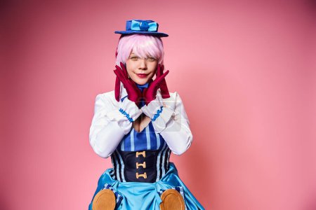 Photo for Attractive chic female cosplayer in blue hat and vivid dress looking at camera on pink backdrop - Royalty Free Image