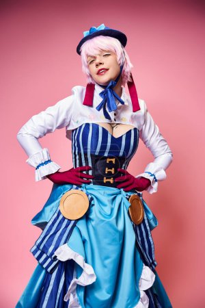 alluring modish female cosplayer in blue hat and vivid dress looking at camera with arms on hips