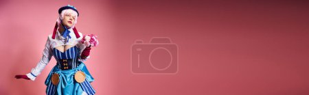 Photo for Cute female cosplayer in vivid attire holding pink flowers and looking away on pink backdrop, banner - Royalty Free Image