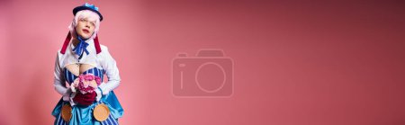 Téléchargez les photos : Cosplayer modish en tenue vibrante tenant des fleurs roses et regardant loin sur fond rose, bannière - en image libre de droit