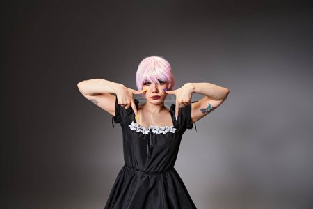 Photo for Good looking female cosplayer in black sexy dress showing crying gestures and looking at camera - Royalty Free Image