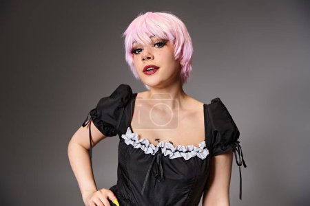 Photo for Pretty alluring cosplayer in sexy maid costume with pink hair looking at camera on gray backdrop - Royalty Free Image