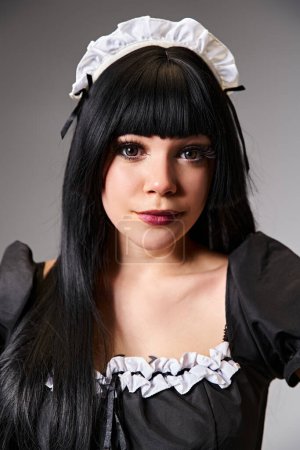 enchanting sexy female cosplayer in tempting maid costume looking at camera on gray background