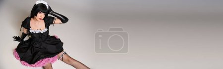 Photo for Sexy young woman in black maid costume cosplaying and looking away on gray backdrop, banner - Royalty Free Image
