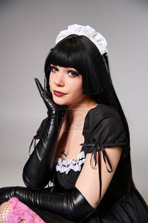 glamorous sexy female cosplayer in tempting maid costume looking at camera on gray background