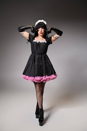Foto de Cosplayer sexy de moda en traje de criada mostrando gesto de llanto y mirando hacia otro lado en el fondo gris - Imagen libre de derechos