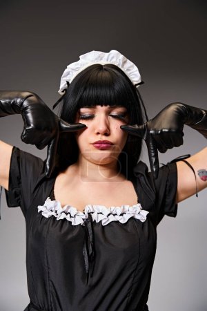 Foto de Atractiva mujer sexy en tentador traje de criada posando con los ojos cerrados y mostrando gesto de llanto - Imagen libre de derechos