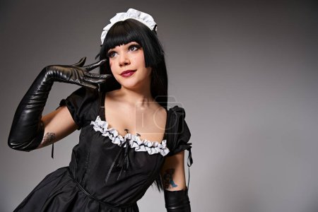 appealing young cosplayer in maid costume posing alluringly and looking away on gray backdrop