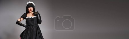 sexy attraktive Cosplayerin im Dienstmädchenkostüm posiert verführerisch und schaut vor grauem Hintergrund weg