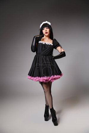 sexy appealing cosplayer in maid costume posing alluringly and looking away on gray backdrop