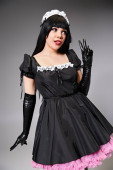 appealing cosplayer in maid costume showing peace gesture and looking away on gray background Stickers #699820510