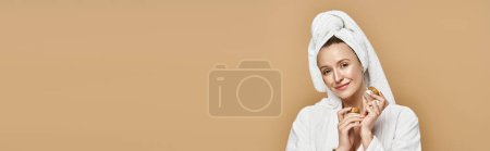 Foto de Una mujer hermosa naturalmente sostiene juguetonamente la crema, con una toalla envuelta alrededor de su cabeza. - Imagen libre de derechos