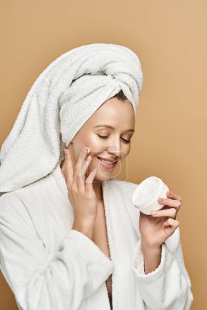 Una hermosa mujer con una toalla envuelta alrededor de su cabeza sostiene un frasco de crema, exudando belleza natural y elegancia.