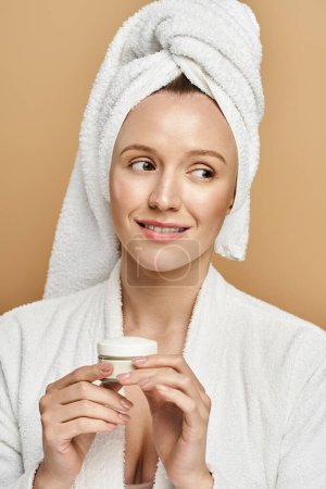 A natural beauty smirking glamorously, with a towel wrapped around her head, holding jar of cream close to her heart.