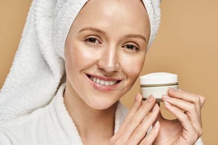 Una mujer con una toalla en la cabeza sostiene un frasco de crema, encarnando la belleza natural y disfrutando de una rutina de autocuidado.