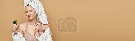 Photo for An attractive woman with a towel on her head holds face roller. - Royalty Free Image
