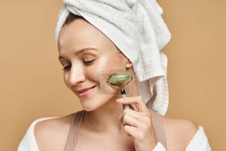 A graceful woman with a towel on her head is seen holding face roller in a poised manner.