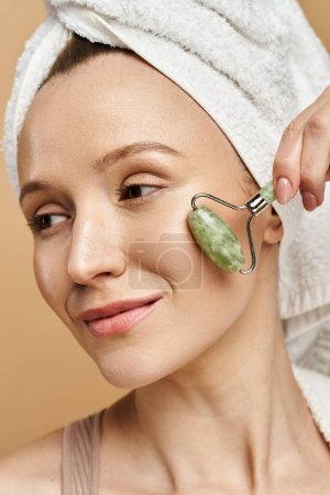 A woman with a towel on her head indulges in self-care with a face roller, radiating tranquility and natural beauty.