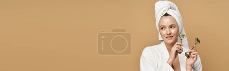 Photo for A woman with a towel on her head delicately holds face roller, exuding natural beauty and grace. - Royalty Free Image