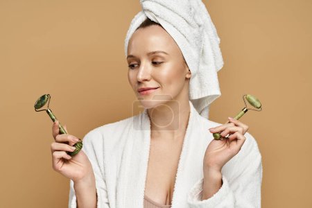 A woman with a towel on her head delicately holding face roller, exuding natural beauty and elegance.