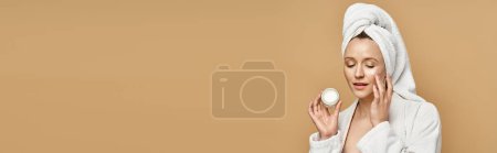 Photo for A woman with a towel on her head holding cream, exuding natural beauty and tranquility during a bath ritual. - Royalty Free Image