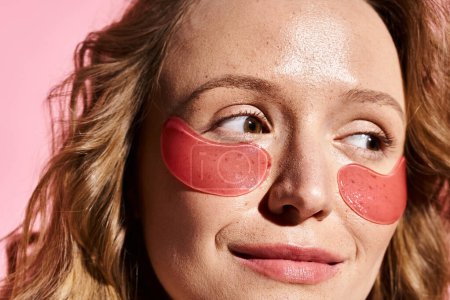 A captivating woman with natural beauty posing gracefully while wearing a pair of pink eye patches on her face.