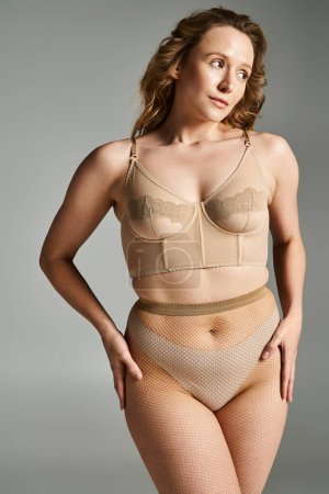 A natural beauty striking a pose in a tan bra and fishnet panty with elegance and allure.