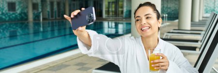 Foto de Una joven morena captura un momento sereno junto a la piscina, levantando un teléfono celular para tomar una foto. - Imagen libre de derechos